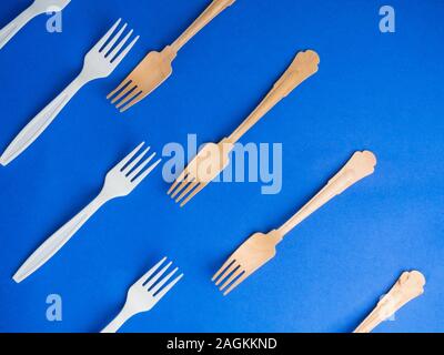 Organic bamboo disposable forks vs plastic ones on trendy blue background. Environmentally friendly wooden and non-oragnic plasticforks Stock Photo