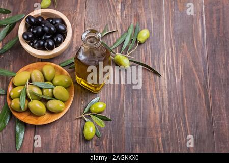 Two kinds of marinated olives, olive oil and branches on the wooden table Stock Photo