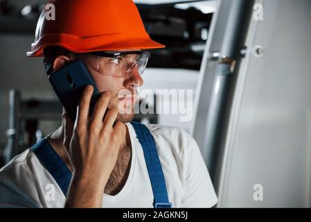 Using phone. Portrait of engineer in metallurgical factory in protective helmet and eyewear Stock Photo