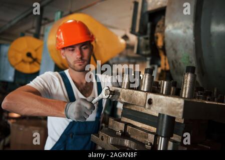 Tightens details of machine by wrench. Man in uniform works on the production. Industrial modern technology Stock Photo