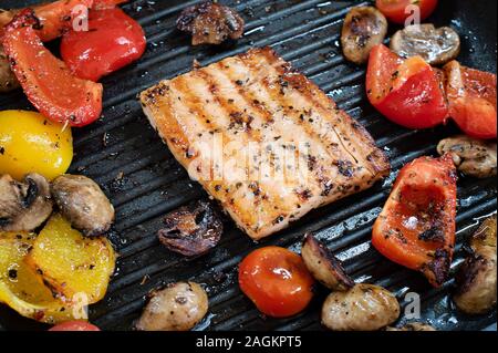 Delicious red fish - salmon and vegetables on the grill. Closeup on grilling square shape salmon, red and yellow peppers, cherry tomatoes and mushroom Stock Photo
