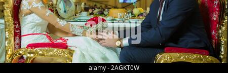 Wedding bouquet in the hands of the bride and groom of roses . sitting in a golden chair in the restaurant. a groom is giving a wedding bouquet of red Stock Photo