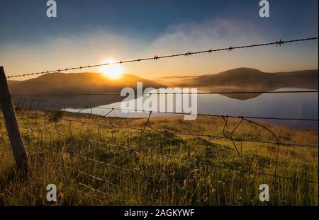 Hills reflected in loch at sunrise and barbed wire fence, Isle of Lewis, Outer Hebrides, Scotland Stock Photo