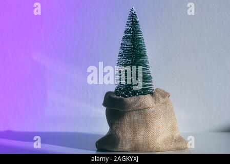 Zero Waste Christmas. Christmas tree in fabric bag in vivid gradient neon colors. Minimal background concept. Stock Photo
