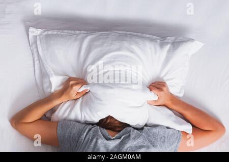 Woman lying on the bed and covering her head with pillow. Stock Photo