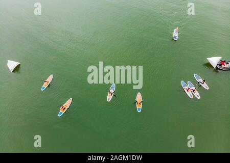 Strong men floating on a SUP boards in a beautiful bay on a sunny day. Aerial view of the men crosses the bay using the paddleboard. Water sports Stock Photo