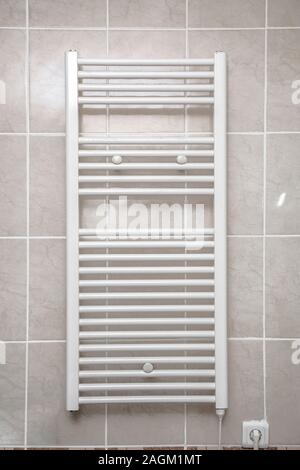 Stainless electric towel dryer for the bathroom. Drying is mounted on a wall with tiles. Towel dryer for drying towels in the bathroom Stock Photo