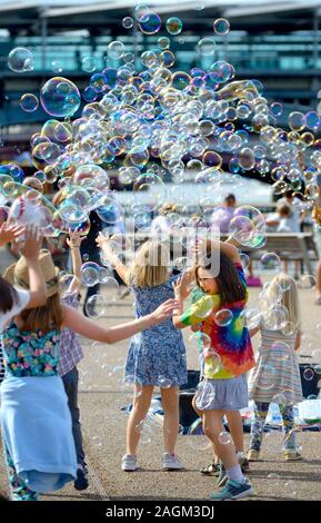 London, England, UK. Children playing with bubbles made by a man making bubbles for children to play with, on the South Bank Stock Photo