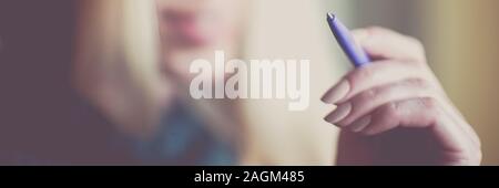 Female hand with pen in air, smiling face background, soft selective focus. Stock Photo