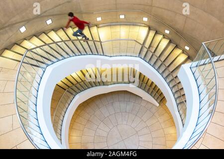 A young man in a red pullover running up a spiral staircase in a garage in Liverpool One shopping centre Stock Photo