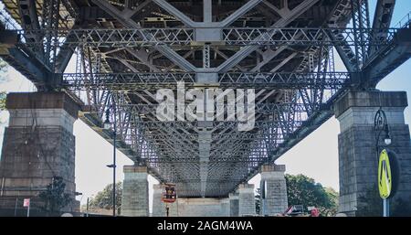 A underneath view of the structure of the Sydney Harbour bridge made up of steel beams and girders sat on concrete Granite faced pillars Stock Photo