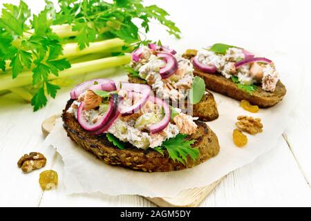 Salmon, petiole celery, raisins, walnuts, red onions and curd cheese salad on toasted bread with green lettuce on paper on a wooden board background Stock Photo