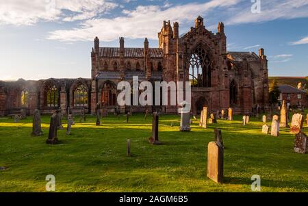 Melrose, Scotland, UK - May 28, 2011: Evening sun casts long shadows across the ruins of Melrose Abbey and gravestones in the abbey churchyard. Stock Photo