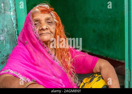 UDAIPUR, INDIA - OCTOBER 28, 2019: Portrait of lderly woman in colorful hair and traditional Rajasthani clothes sitting in front of door in vegetable Stock Photo