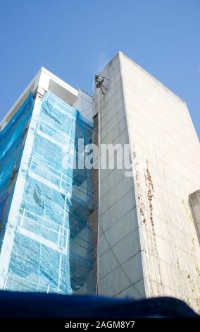 Rope access technician washing building facade. Cleaning service at height concept Stock Photo