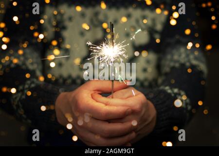 Man in sweater with deers holding bright festive Christmas sparkler in hand. Stock Photo