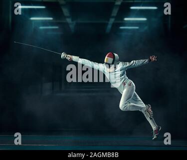 Shallow focus shot of a person fencing  with a fencing mask and an epee in a dark room Stock Photo