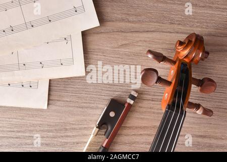 Violin pegbox and bow with sheet music on wood table. Top view. Horizontal composition. Stock Photo