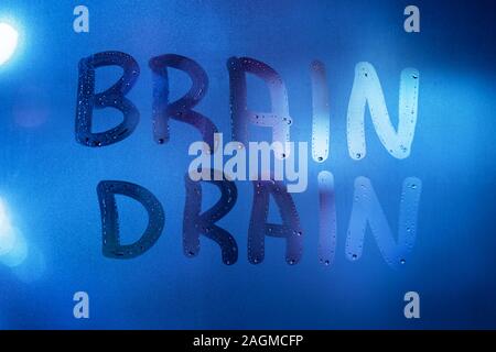 the words brain drain written on night wet window glass close-up with blurred background in classic blue color Stock Photo