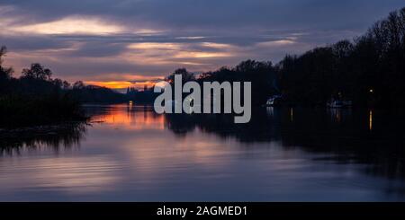 Smoke rises from houseboats moored on the River Thames at sunset between Richmond and Twickenham in west London. Stock Photo