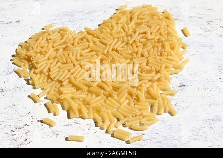 Dry Pasta Background. Uncooked macaroni pasta in the shape of a heart on a white background Stock Photo