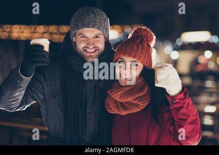 Merry christmas. Photo of two people pair with hot beverage in hands celebrating x-mas evening raising mugs telling toasts wearing warm coats outside Stock Photo