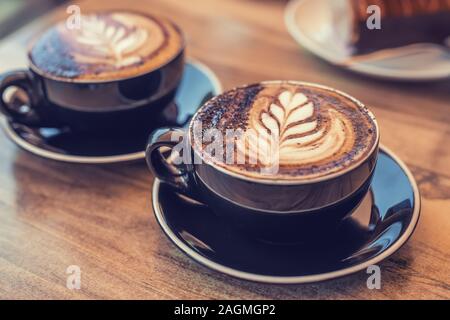 Two black cups of coffee with art on a table, blurred desert on the background