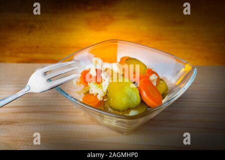 pieces of pickled vegetables, pickles carrots and cabbage in a glass jar with a fork on a wooden table Stock Photo