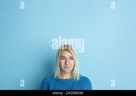 Portrait of young caucasian woman looks dreamful, cute and happy. Thinking, wondering, dreaming on blue studio background. Copyspace for your ad. Concept of future, target, dreams, visualisation. Stock Photo