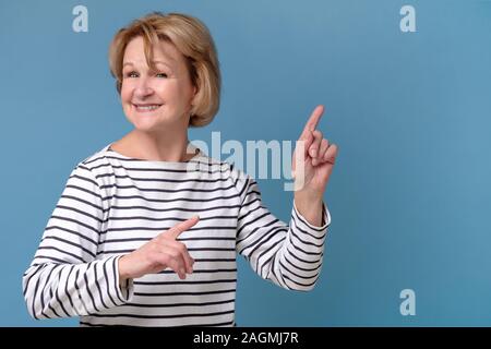 Middle aged woman pointing at copyspace isolated on blue background Stock Photo
