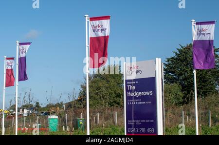 Westergate, West Sussex, UK, October 06, 2019. Taylor Wimpey Flags fluttering in the breeze by the advertising board  entrance to new The Hedgerows. Stock Photo