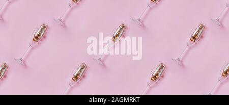 Champagne glasses with golden and red baubles inside on pastel pink background Stock Photo