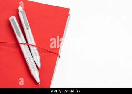 A journal with red leather cover and elastic band securing two metallic ballpoint pens. Stock Photo