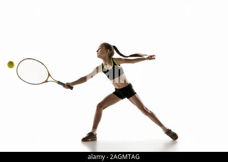 Little caucasian girl playing tennis on white studio background. Cute model training, practicing in motion, action. Youth, flexibility, power and energy. Movement, ad, sport, healthy lifestyle concept. Stock Photo
