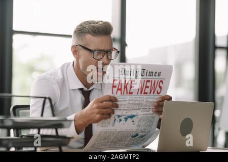 shocked businessman reading newspaper with fake news on pink background ...