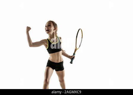 Little caucasian girl playing tennis on white studio background. Cute model emotional celebrating win in motion, action. Youth, flexibility, power and energy. Ad, sport, healthy lifestyle concept. Stock Photo
