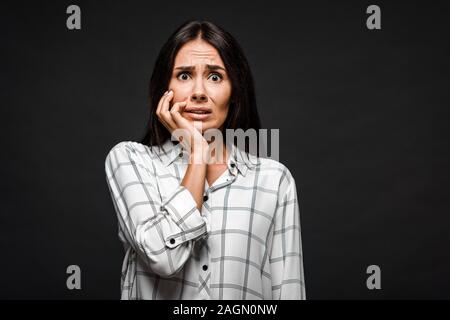 scared woman looking at camera while touching face isolated on black Stock Photo
