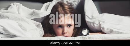 scared child hiding under blanket with flashlight isolated on black Stock Photo