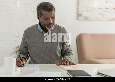 concentrated african american man calculating expenses while writing in utility bill Stock Photo