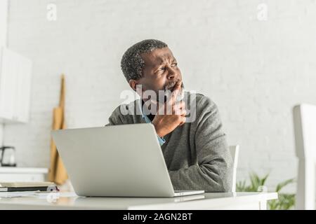 thoughtful african american man looking away while sitting near laptop Stock Photo