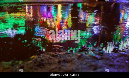 Puddle at night in the rain with reflecting lights at a fair or fun fair Stock Photo