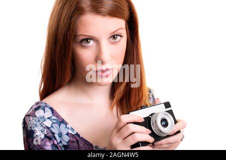 Close up portrait of a beautiful young girl holding a retro film camera in hands while standing and looking at the camera, isolated on white. Stock Photo