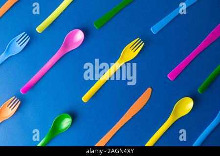 Flat lay of colorful plastic disposable forks,spoons and knives pattern on classic blue background minimal creative concept. Stock Photo