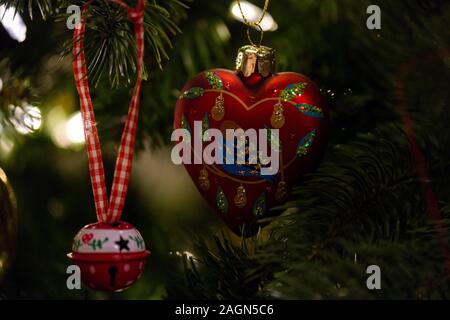 A  heart shaped red Christmas bauble decorated with a partridge and a red bell hanging in a Christmas tree Stock Photo