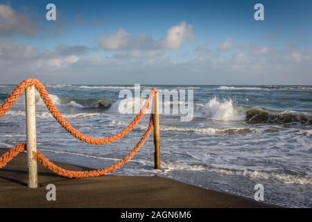 Late afternoon beach, sea edge with rope fence looking out to sea with crashing waves