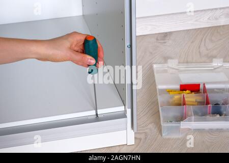 Repairs in house or apartment. Female hand repairing white furniture with a screwdriver in home. Closeup. Diy concept. Stock Photo