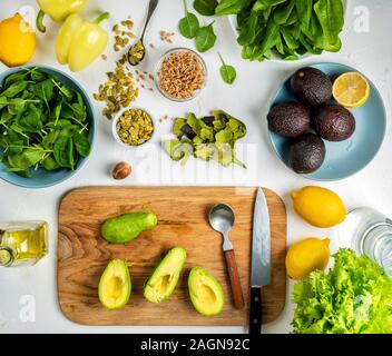 halves of avocado on a wooden board and other healthy diet ingredients on the kitchen table. Top view. Stock Photo