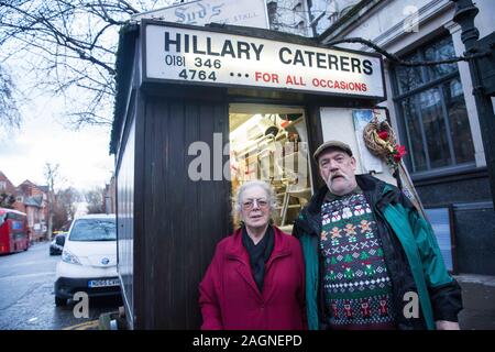 London, UK. 20 December, 2019. Jane Tothill and Syd Tothill Junior, grandchildren of Syd Tothill, pose in front of Syd’s Coffee Stall, which has been run by three generations of the same family on the corner of Shoreditch High Street and Calvert Avenue since 1919, immediately before it was closed for business. The mahogany coffee stall, which has been run by Jane Tothill for thirty years, will go on display in the new Museum of London in Smithfield in 2024. Credit: Mark Kerrison/Alamy Live News Stock Photo