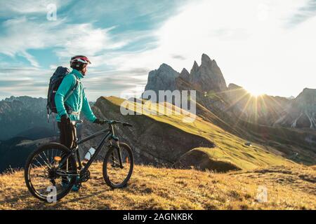 Young man with mountain bike on Seceda mountain peak at sunrise. Puez Odle, Trentino, Dolomites, Italy. Stock Photo