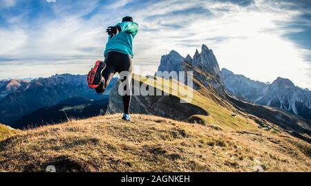 Young man in sport trail clothes running on Seceda mountain peak at sunrise. Puez Odle, Trentino, Dolomites, Italy. Stock Photo